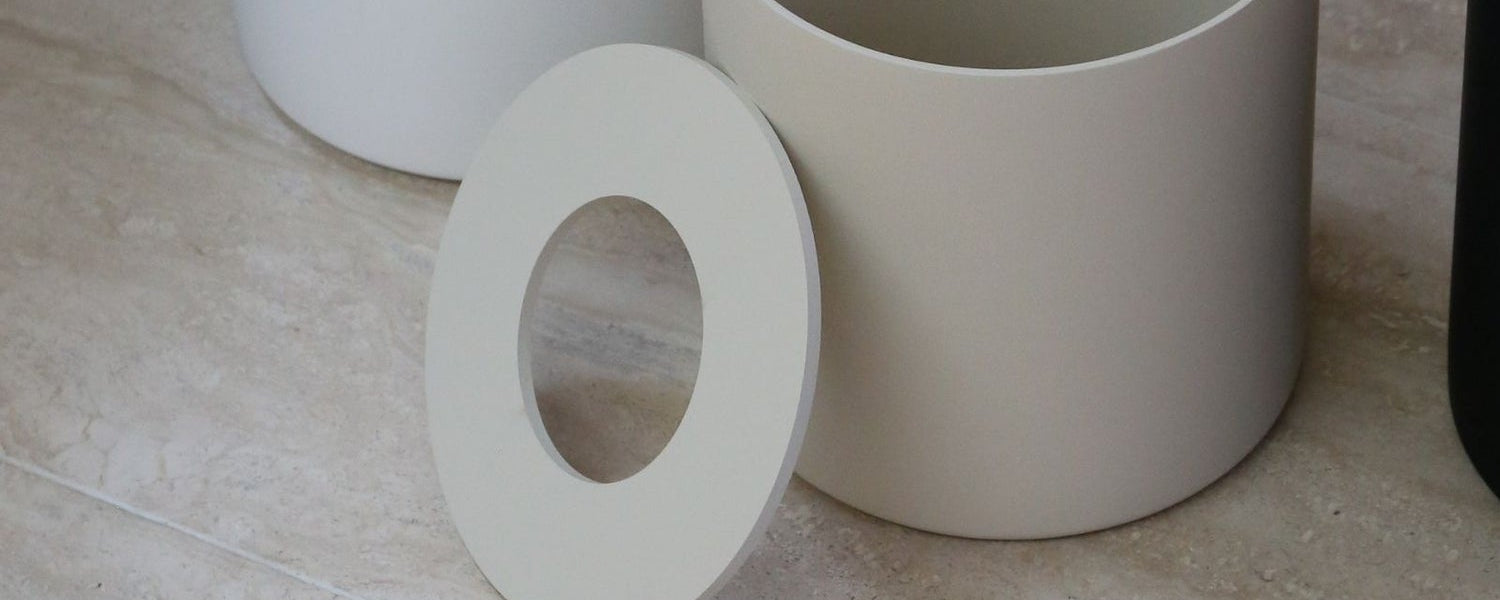 Three cylindrical bins in white, beige, and black on a marble surface.