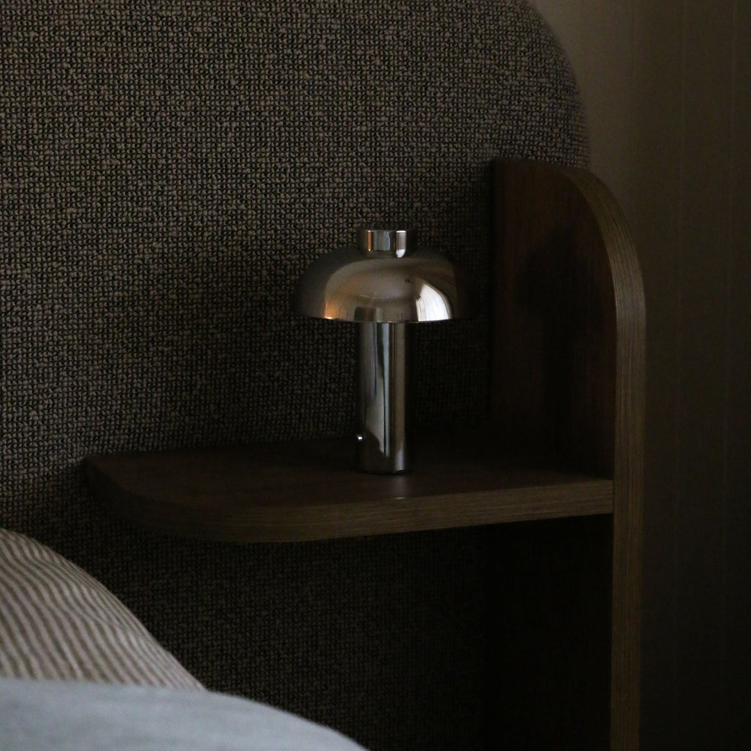 Silver lamp on a wooden nightstand against a textured wall.