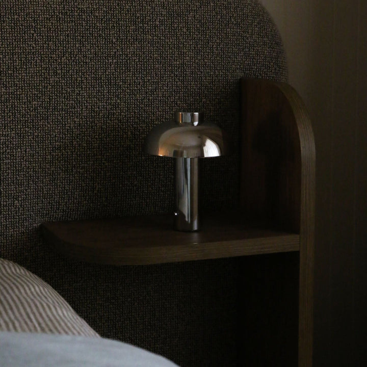 Silver lamp on a wooden nightstand against a textured wall.