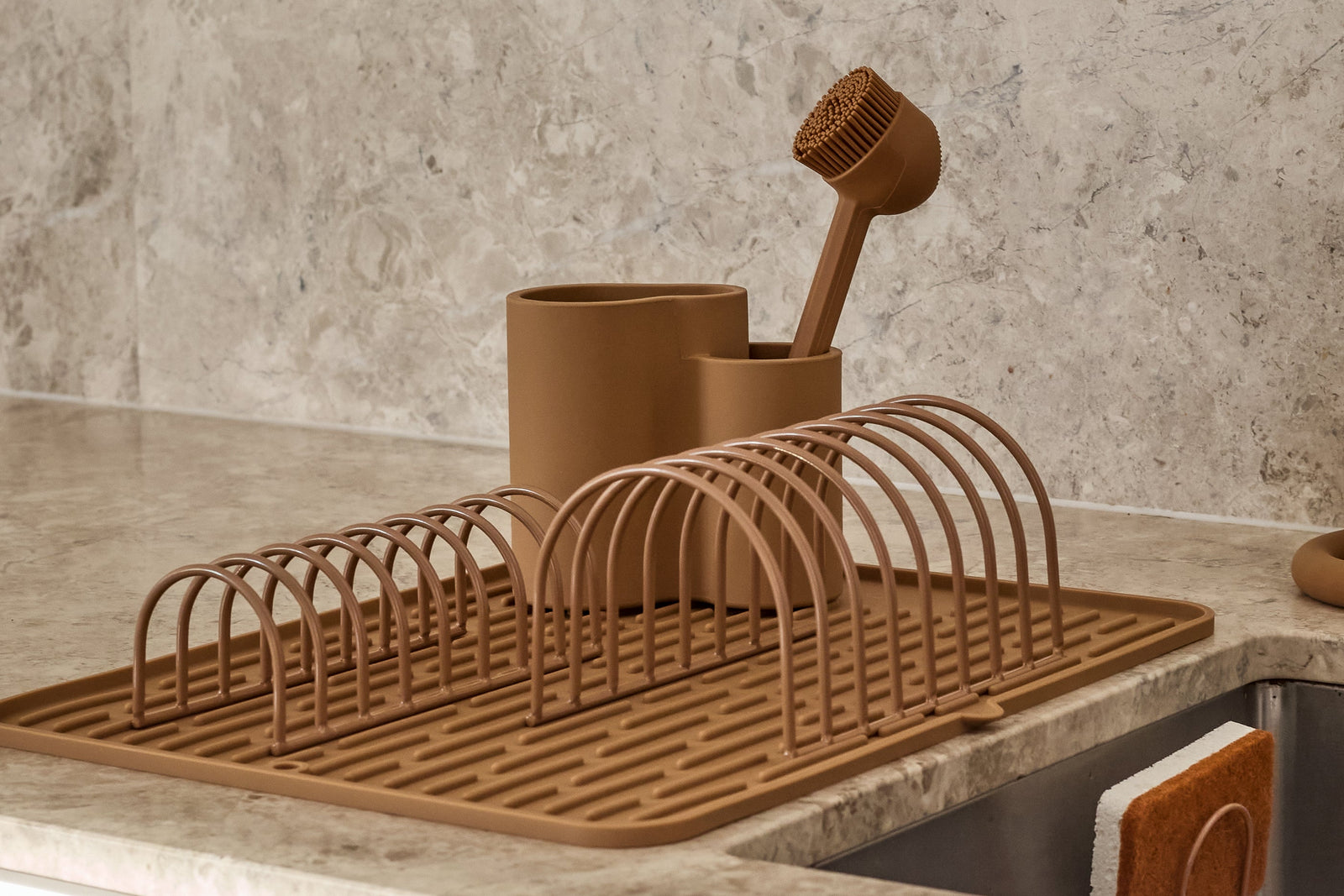 Kitchen sink area with a drying rack, cups, and bottles on a countertop.